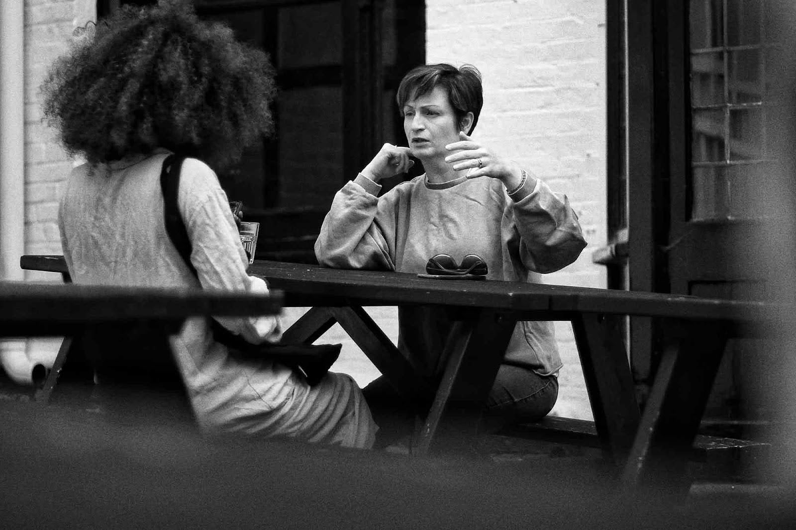 Two women, talking, sitting, picnic bench.